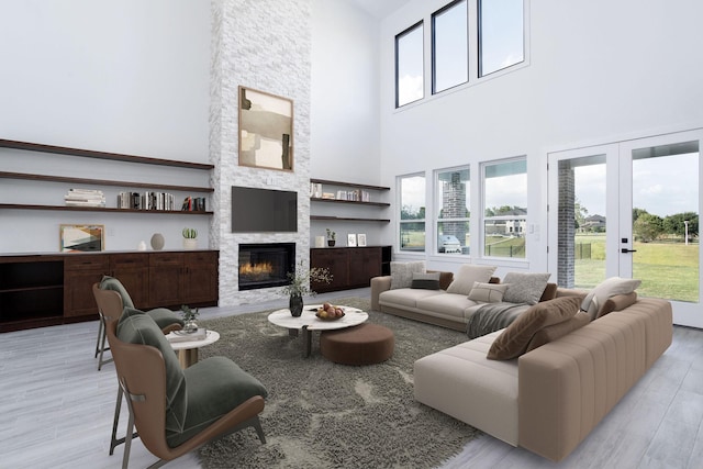 living room featuring a fireplace, a towering ceiling, light wood-type flooring, and french doors