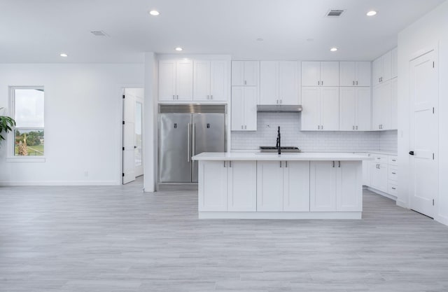 kitchen with light hardwood / wood-style flooring, white cabinetry, stainless steel built in fridge, and an island with sink