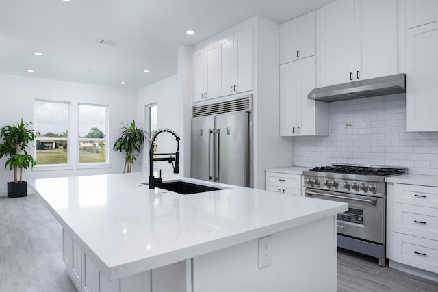 kitchen featuring sink, light stone counters, high quality appliances, a center island with sink, and light wood-type flooring