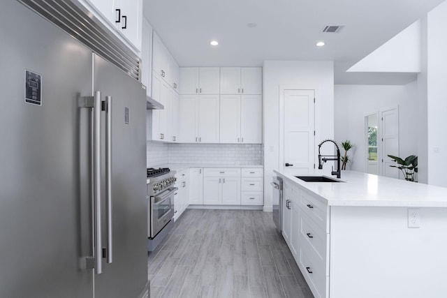 kitchen with sink, light hardwood / wood-style flooring, an island with sink, premium appliances, and white cabinetry