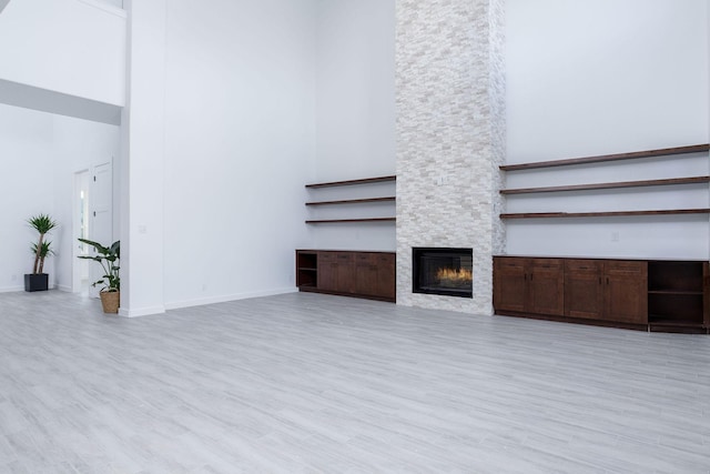 unfurnished living room featuring a stone fireplace, a high ceiling, and light hardwood / wood-style flooring