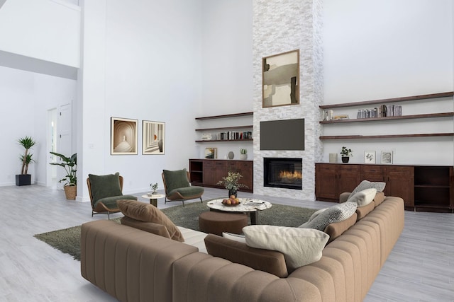 living room with a fireplace, a towering ceiling, and light hardwood / wood-style flooring