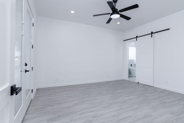 empty room with a barn door, light hardwood / wood-style floors, and ceiling fan