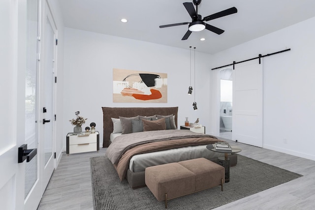 bedroom featuring light wood-type flooring, a barn door, ensuite bath, and ceiling fan