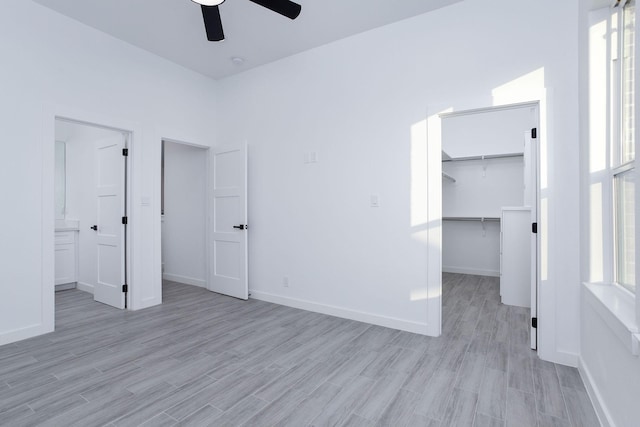 unfurnished bedroom featuring a walk in closet, light hardwood / wood-style flooring, a closet, and ceiling fan