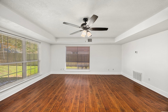 unfurnished room with a textured ceiling, ceiling fan, a raised ceiling, and dark wood-type flooring