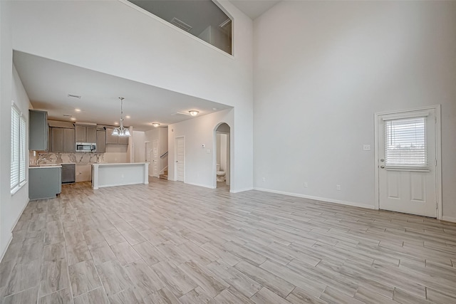 unfurnished living room featuring light wood-type flooring, a towering ceiling, and a chandelier