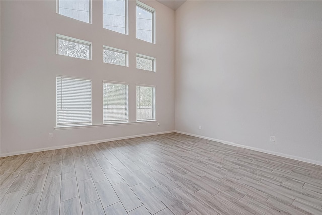 unfurnished room with light hardwood / wood-style flooring, a towering ceiling, and plenty of natural light