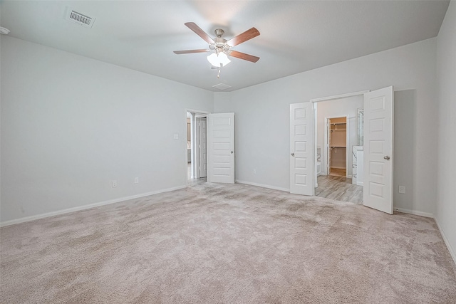 unfurnished bedroom featuring ceiling fan, a walk in closet, and light carpet