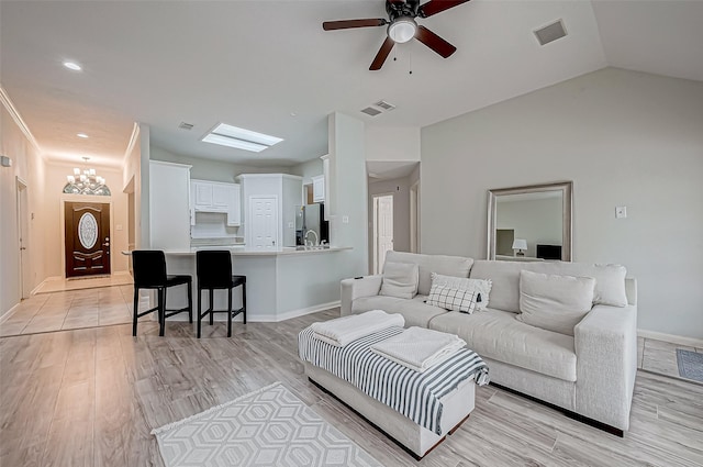 living room with vaulted ceiling, light hardwood / wood-style floors, and ceiling fan with notable chandelier