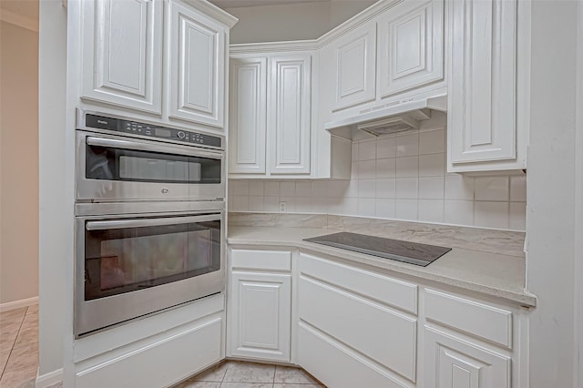 kitchen featuring black electric stovetop, tasteful backsplash, stainless steel double oven, light tile patterned floors, and white cabinetry