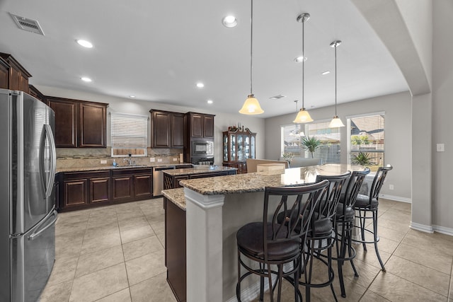 kitchen with pendant lighting, backsplash, light stone countertops, appliances with stainless steel finishes, and a kitchen island