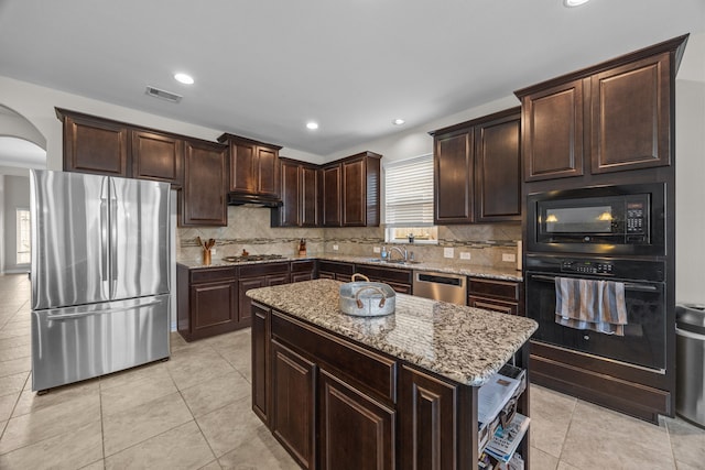 kitchen with black appliances, a kitchen island, light stone counters, and a wealth of natural light