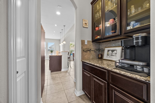 kitchen featuring tasteful backsplash, light stone counters, dark brown cabinets, light tile patterned floors, and decorative light fixtures