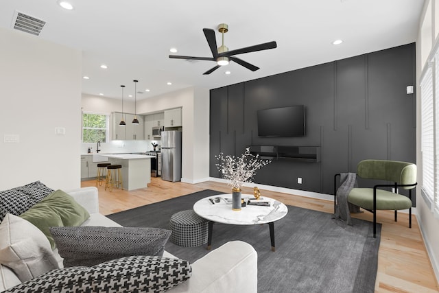 living room featuring ceiling fan, sink, and light wood-type flooring