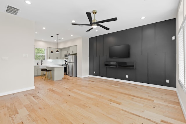 unfurnished living room with light hardwood / wood-style flooring, ceiling fan, and sink