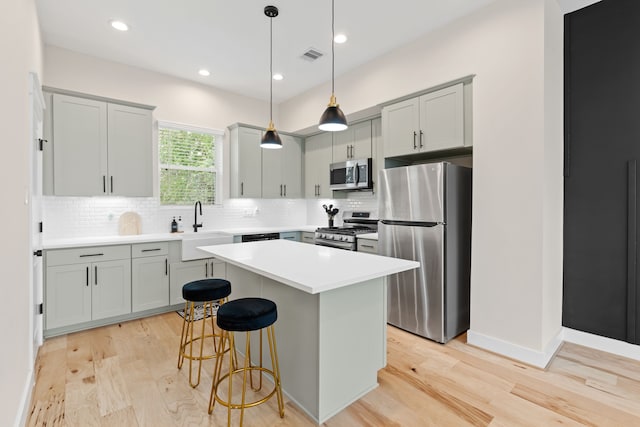 kitchen with a kitchen bar, appliances with stainless steel finishes, pendant lighting, light hardwood / wood-style flooring, and a kitchen island