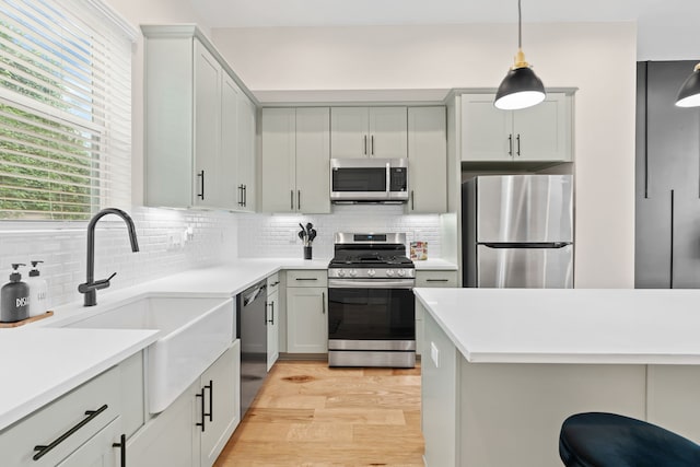 kitchen with backsplash, stainless steel appliances, sink, pendant lighting, and light hardwood / wood-style floors