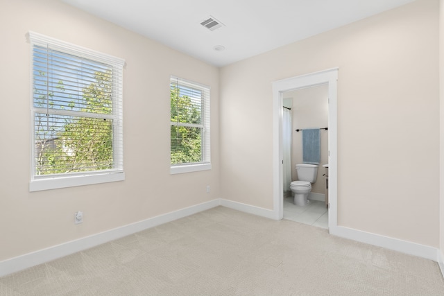 unfurnished bedroom featuring light colored carpet and ensuite bath