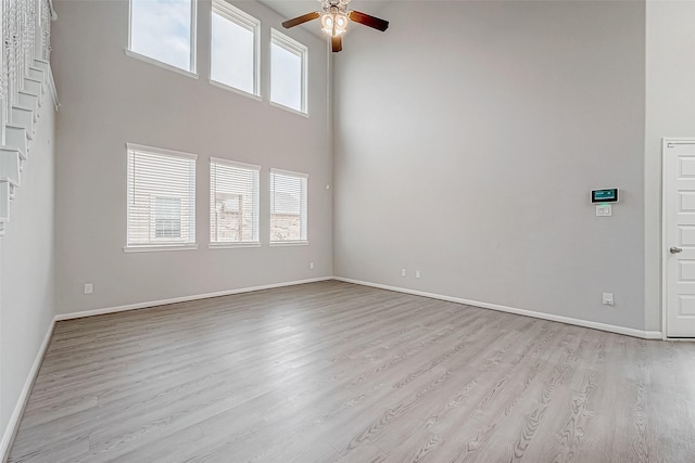 unfurnished living room with ceiling fan, a healthy amount of sunlight, a high ceiling, and light hardwood / wood-style flooring