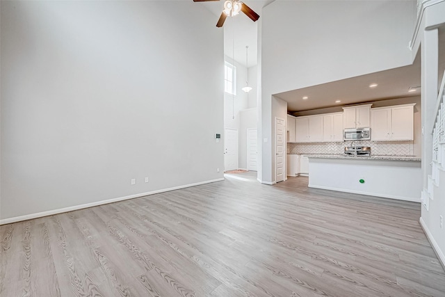 unfurnished living room featuring a towering ceiling, light hardwood / wood-style flooring, and ceiling fan