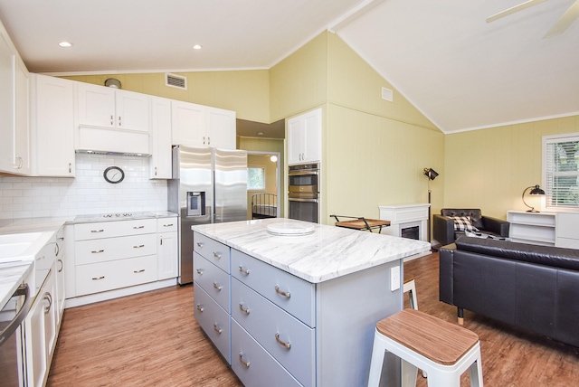 kitchen featuring stainless steel appliances, vaulted ceiling, white cabinetry, light hardwood / wood-style floors, and a kitchen island