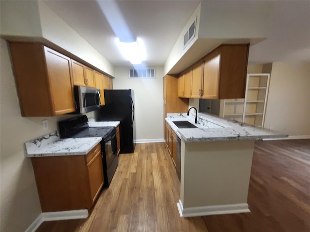 kitchen featuring visible vents, light stone counters, a peninsula, black appliances, and a sink