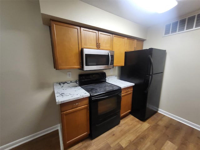 kitchen with black appliances, light wood-style flooring, brown cabinetry, and visible vents