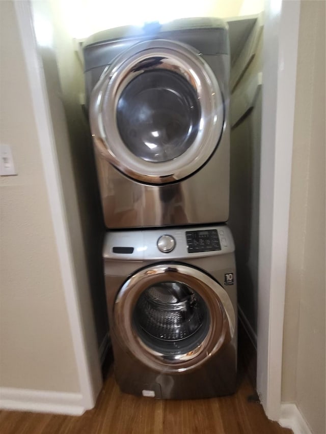 laundry area with stacked washer / drying machine, laundry area, baseboards, and wood finished floors