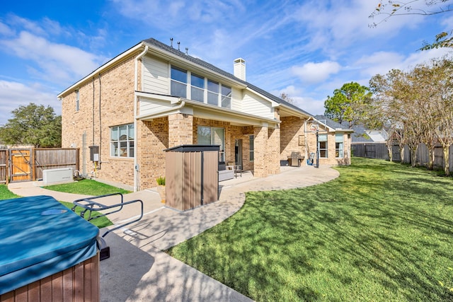 back of property with a lawn, a patio, and a hot tub