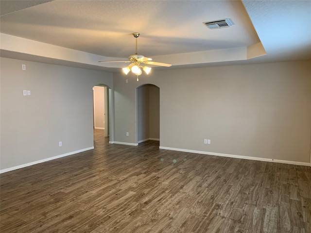 unfurnished room with ceiling fan, a raised ceiling, and dark wood-type flooring