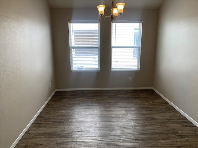 spare room with a notable chandelier and dark wood-type flooring