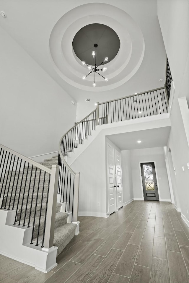 entrance foyer with a high ceiling, hardwood / wood-style flooring, a tray ceiling, and a notable chandelier