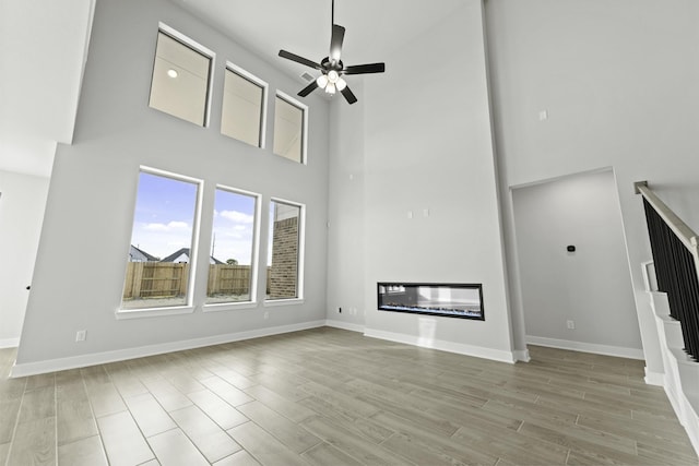 unfurnished living room with a high ceiling, light hardwood / wood-style floors, and ceiling fan