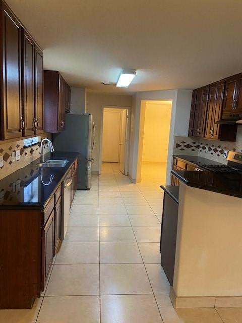 kitchen featuring tasteful backsplash, dark brown cabinets, ventilation hood, sink, and light tile patterned floors