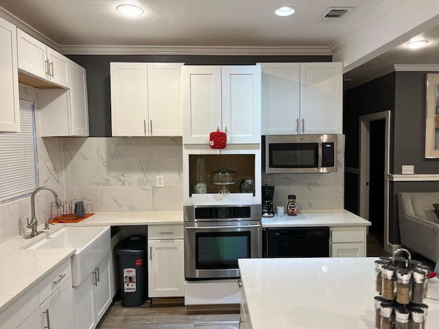 kitchen featuring tasteful backsplash, ornamental molding, stainless steel appliances, sink, and white cabinetry