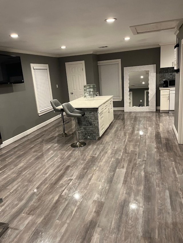 interior space featuring white cabinetry, dark hardwood / wood-style floors, a kitchen bar, a kitchen island, and ornamental molding