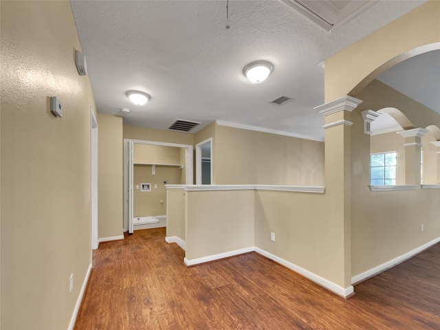 interior space with a textured ceiling, hardwood / wood-style flooring, and ornate columns