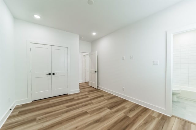 unfurnished bedroom featuring wood-type flooring, ensuite bath, and a closet