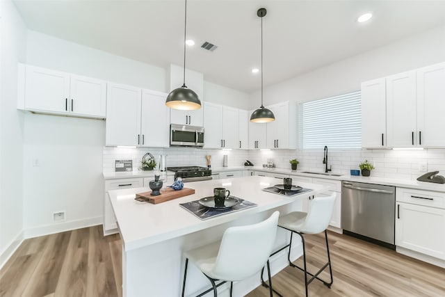 kitchen with white cabinets, sink, hanging light fixtures, a kitchen island, and stainless steel appliances