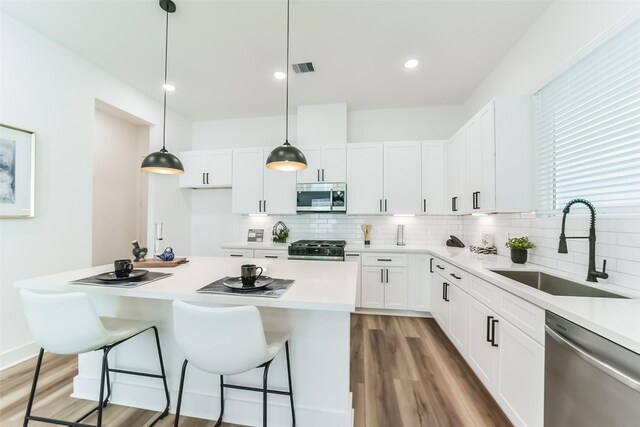 kitchen featuring white cabinetry, sink, hanging light fixtures, a kitchen breakfast bar, and appliances with stainless steel finishes