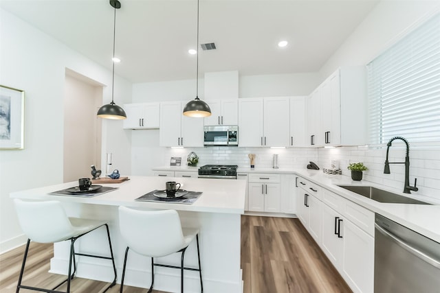 kitchen featuring hanging light fixtures, stainless steel appliances, white cabinets, sink, and a kitchen bar