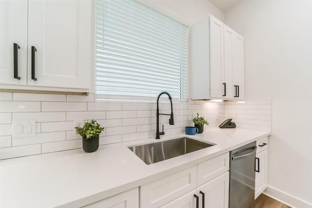 kitchen featuring backsplash, stainless steel dishwasher, sink, hardwood / wood-style flooring, and white cabinetry