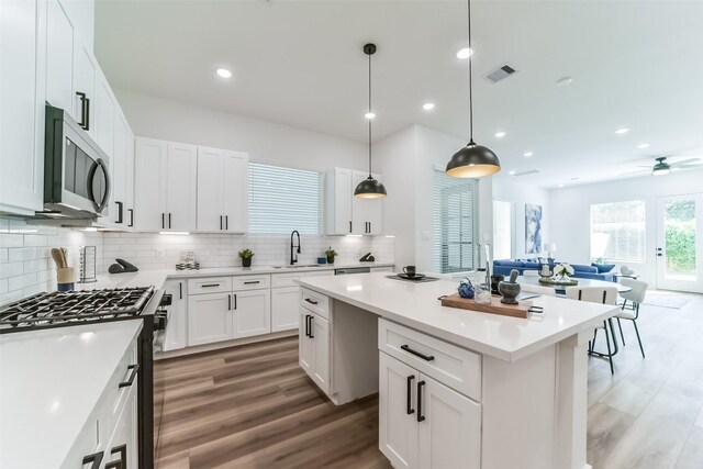 kitchen with white cabinetry, dark wood-type flooring, decorative light fixtures, a kitchen island, and appliances with stainless steel finishes