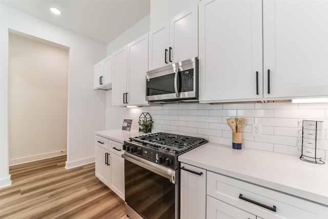 kitchen with appliances with stainless steel finishes, white cabinets, decorative backsplash, and light hardwood / wood-style flooring