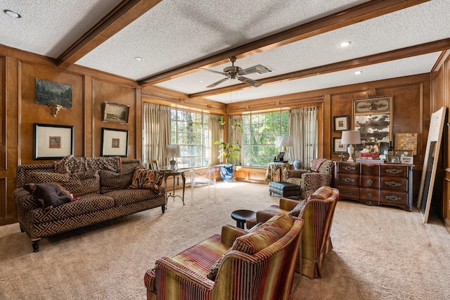 carpeted living room featuring ceiling fan, a textured ceiling, beamed ceiling, and wood walls