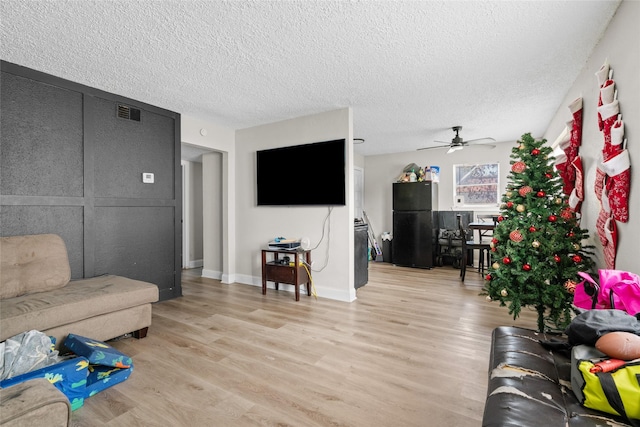 living room featuring ceiling fan, light hardwood / wood-style flooring, and a textured ceiling