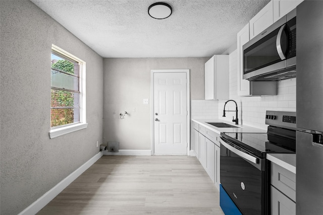 kitchen with sink, tasteful backsplash, light hardwood / wood-style flooring, white cabinets, and appliances with stainless steel finishes