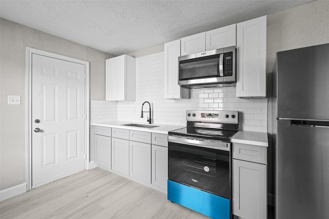 kitchen with tasteful backsplash, stainless steel appliances, sink, light hardwood / wood-style flooring, and white cabinets