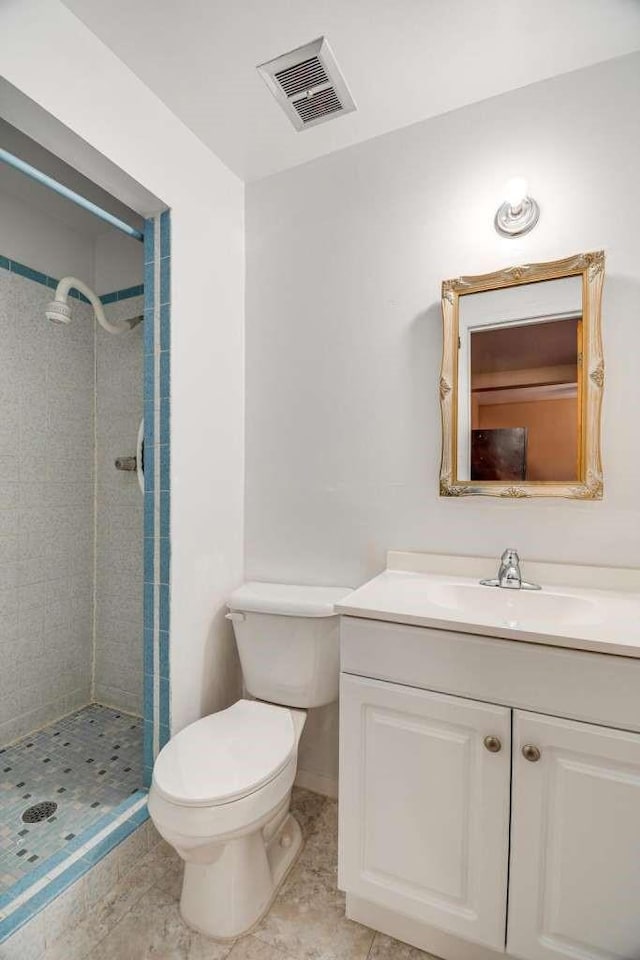 bathroom featuring tile patterned flooring, a tile shower, vanity, and toilet